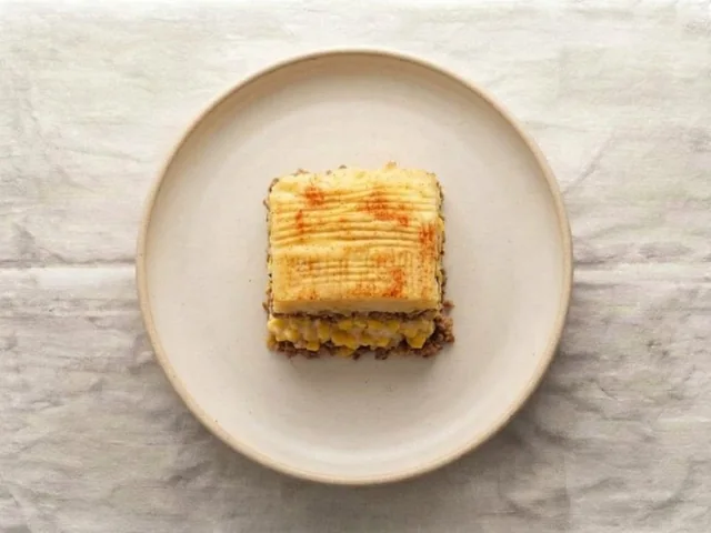 A square of lighter pâté chinois on a plate: mash, creamed corn and beef layers